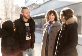 tre kvinnor och en man står utomhus i grupp mannen och en kvinna tittar in i kameran