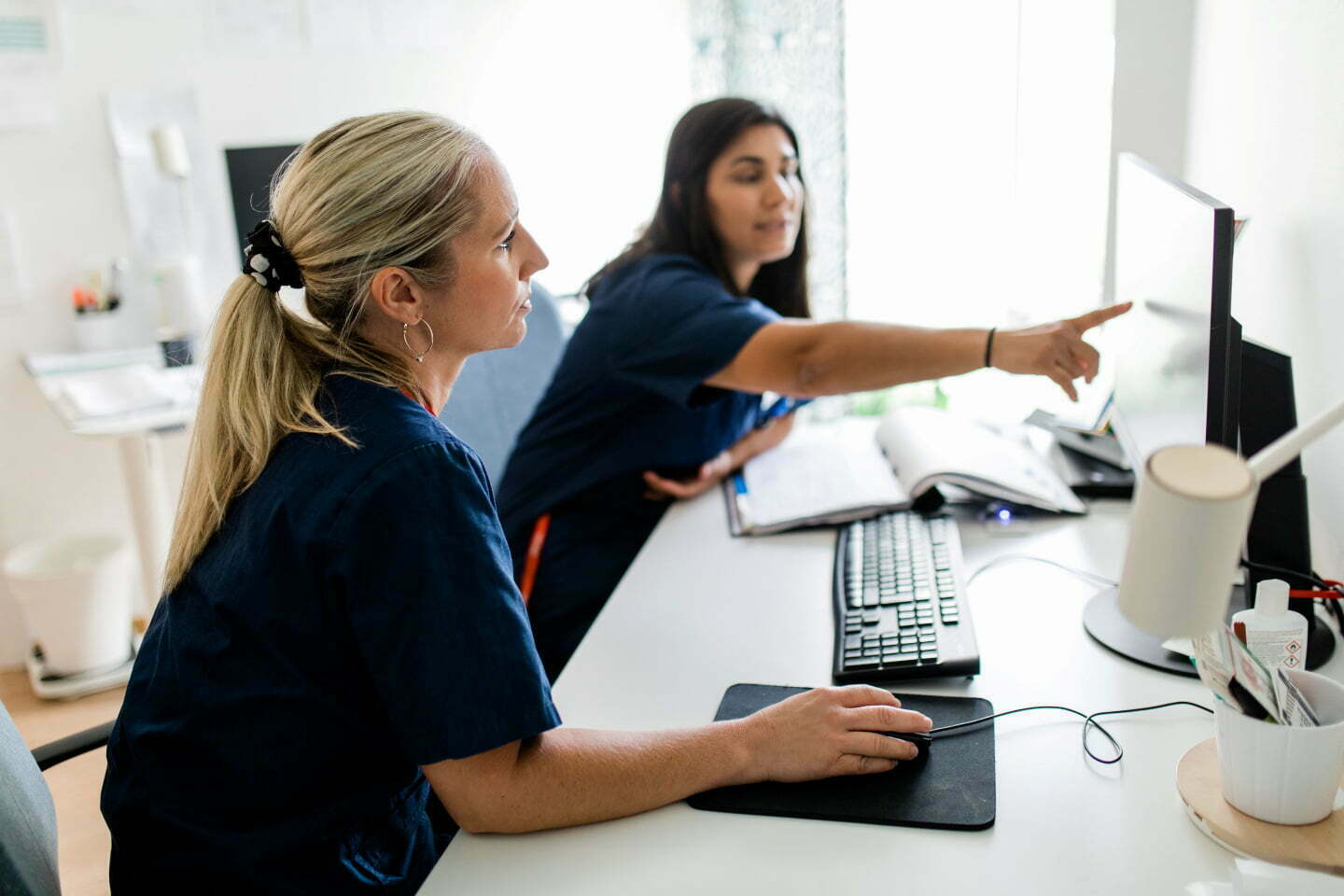 två sjuksköterskor sitter vid bord framför dator