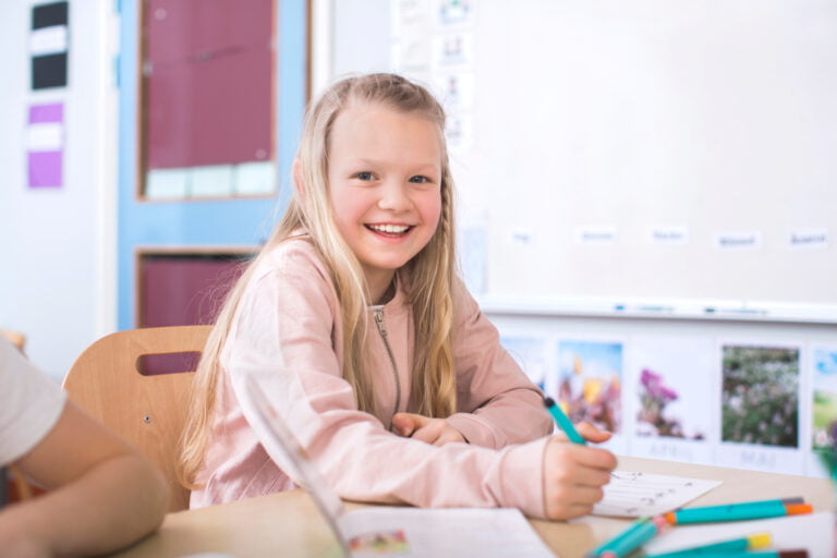 glad flicka sitter i en skolbänk.