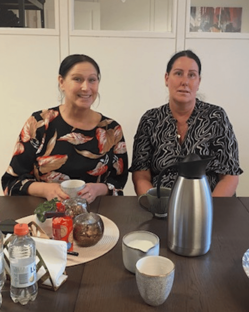 Två kvinnor vid ett bord med frukt och kaffe. 