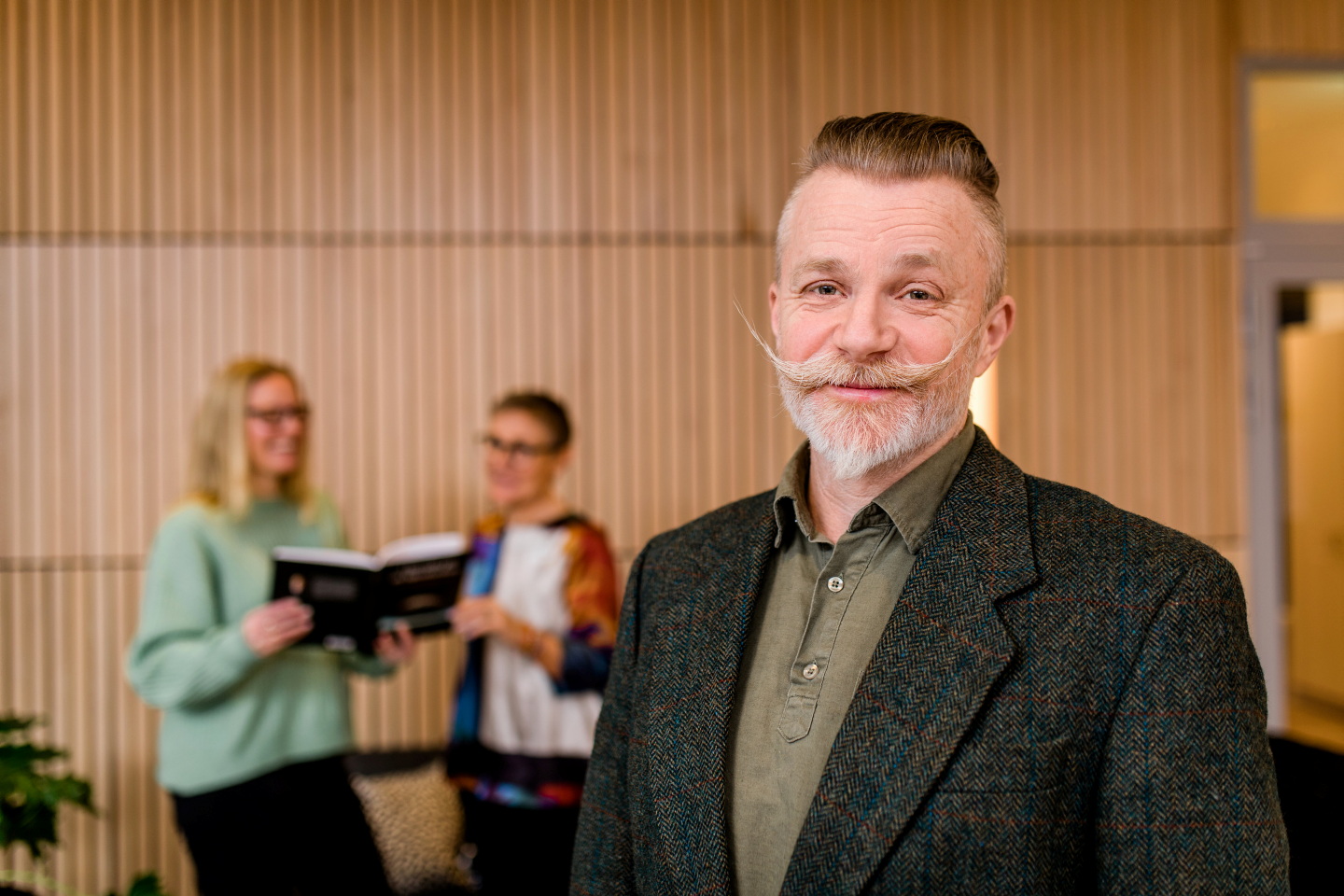 Man som står framför två kvinnor med en bok i ett rum